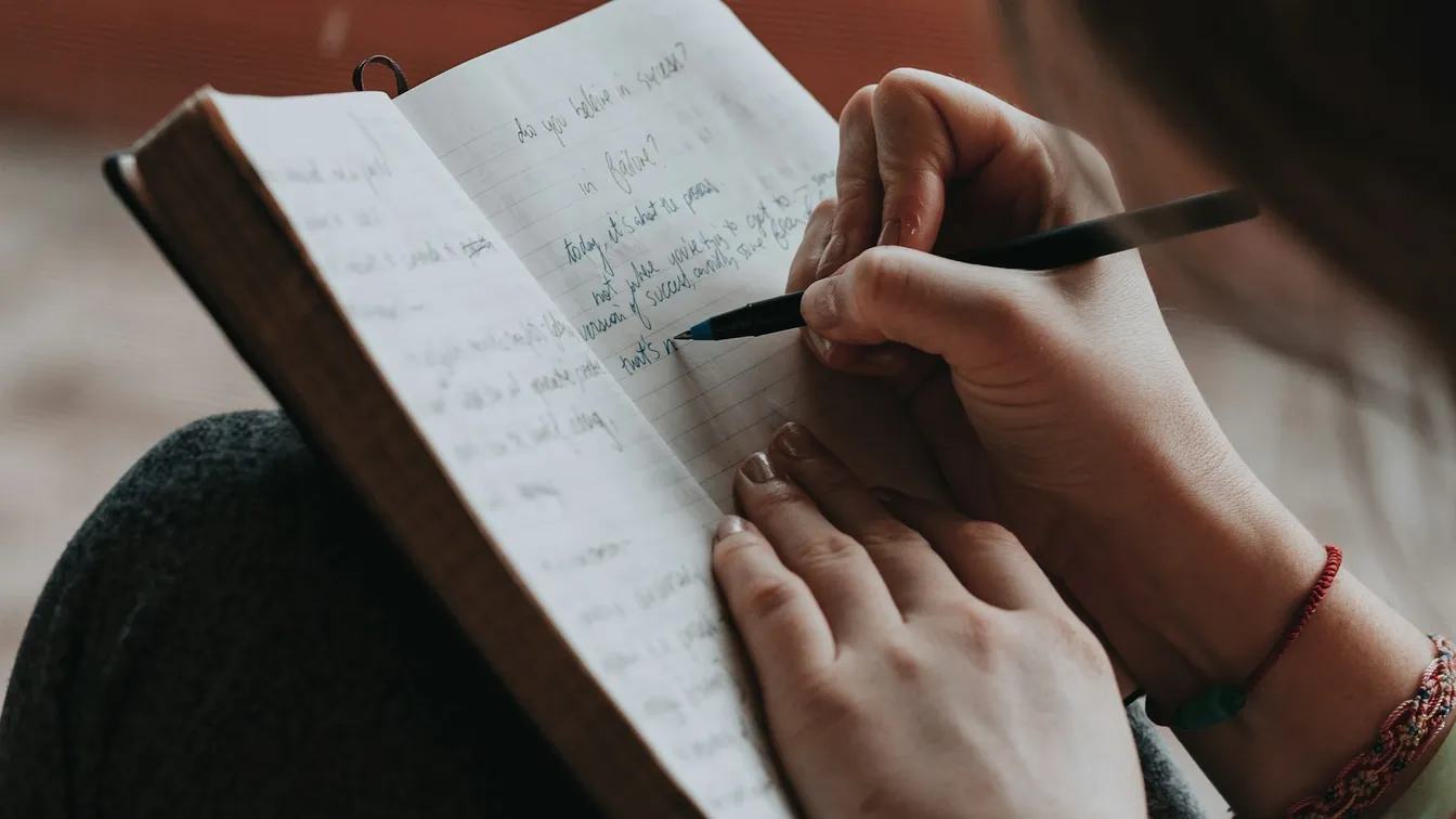 a woman writing in a notebook with a pen