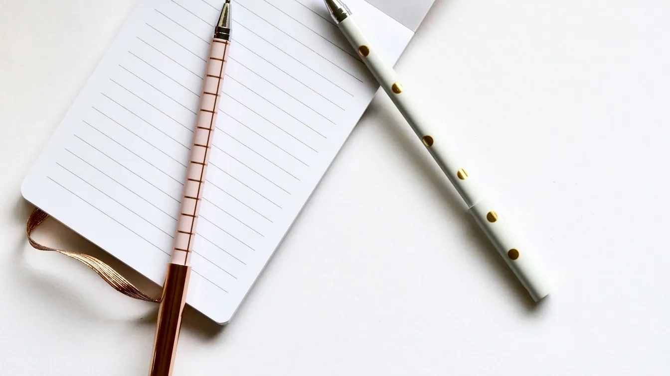 two pens and a notebook on top of a white surface