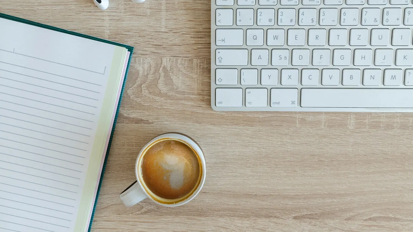 a notebook with a cup of coffee and a keyboard on a desk