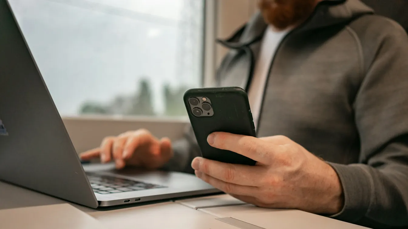 a man using a cell phone while sitting in front of a laptop