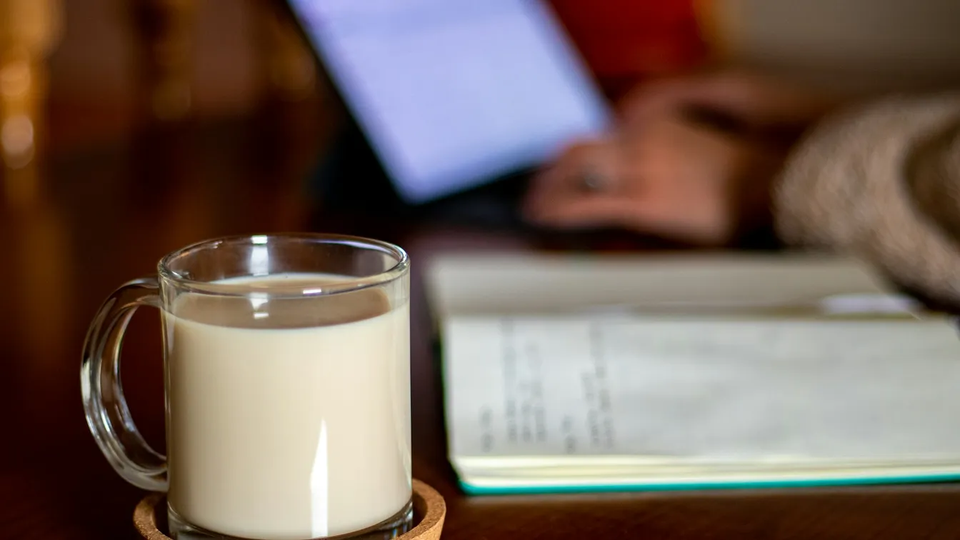 a cup of coffee on a wooden table next to a laptop