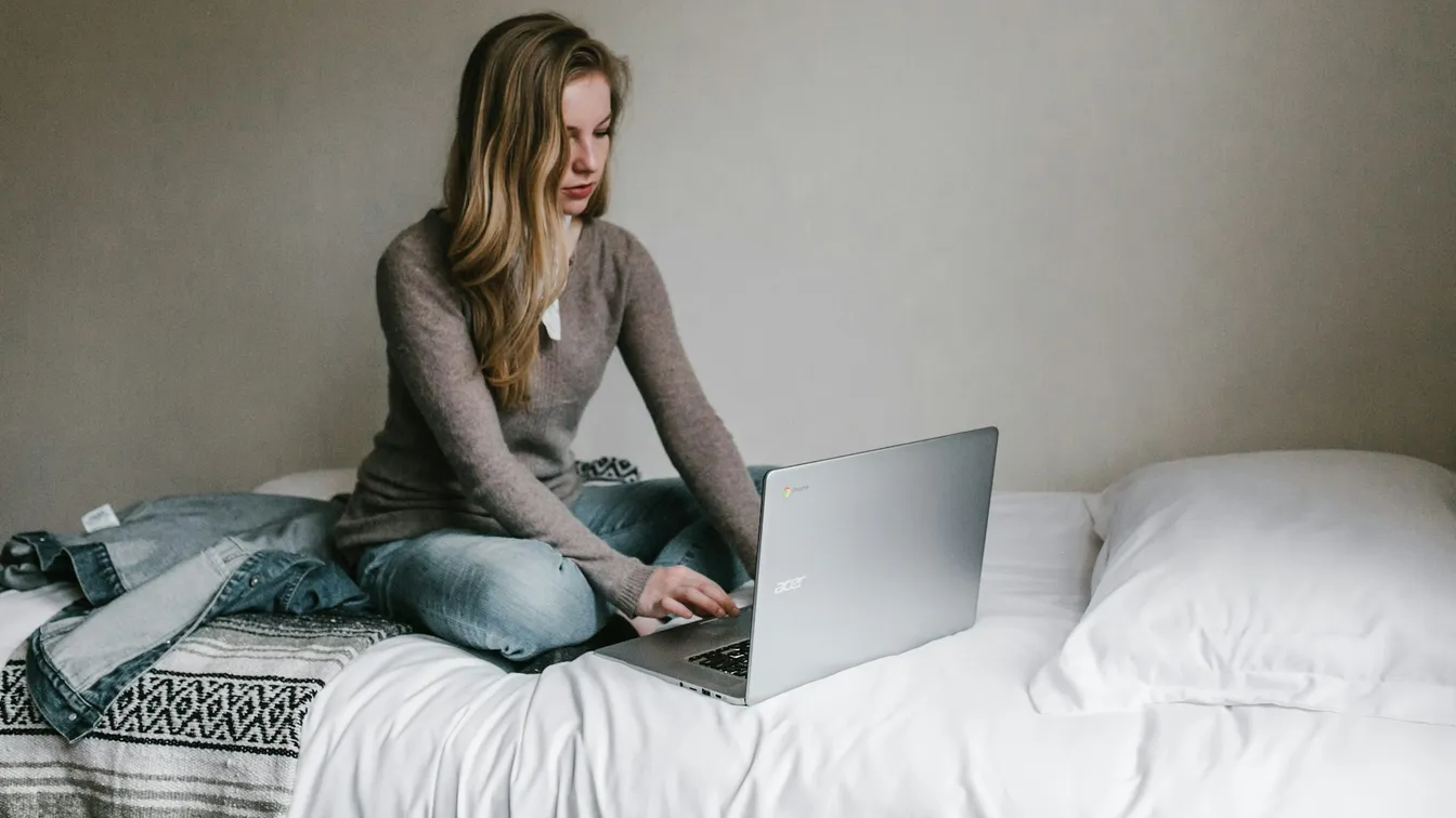 a woman sitting on a bed using a laptop