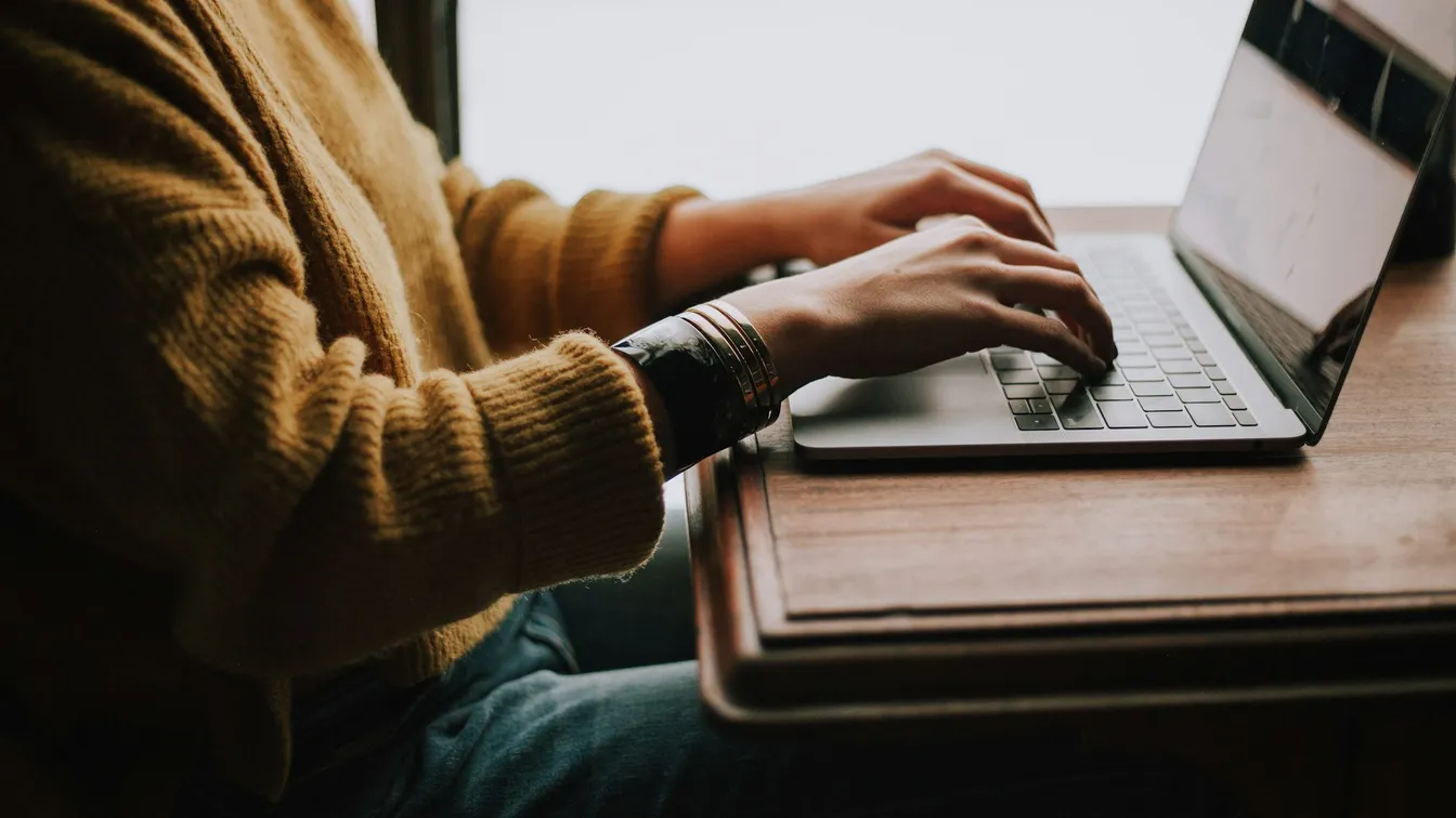 a person typing on a laptop in front of a window