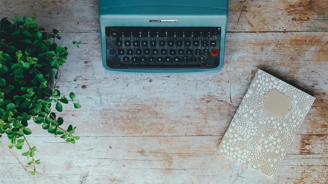 a typewriter sits on a wooden table next to a plant