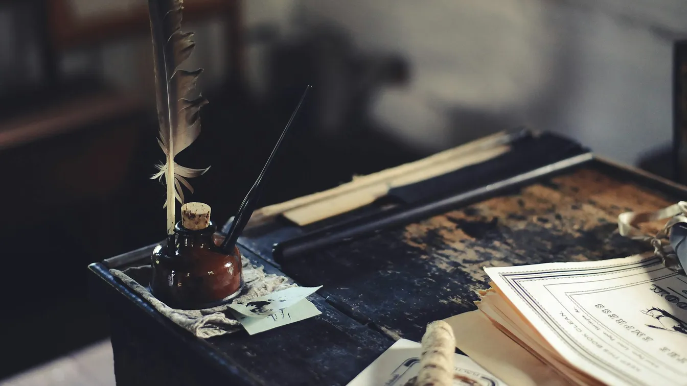 a desk with a pen, ink, and a notebook