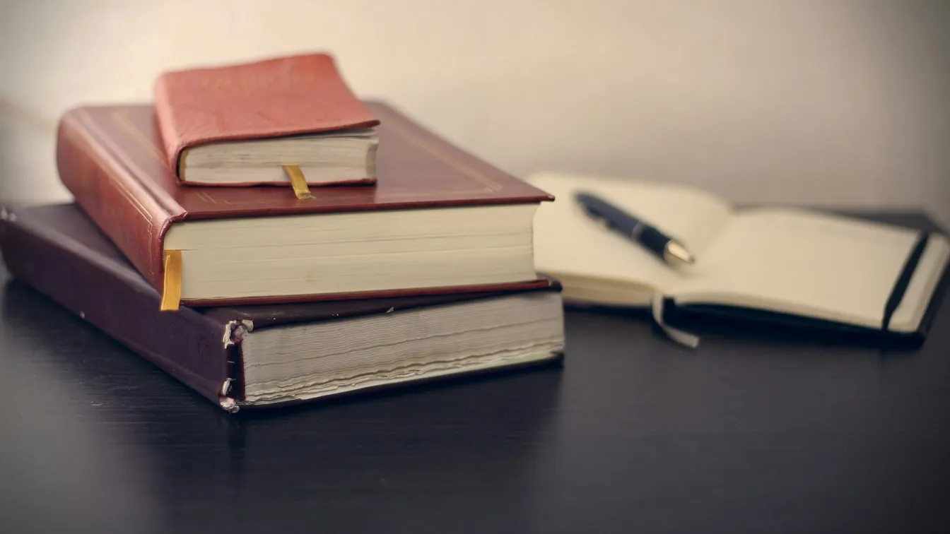 a stack of books and a pen on a table