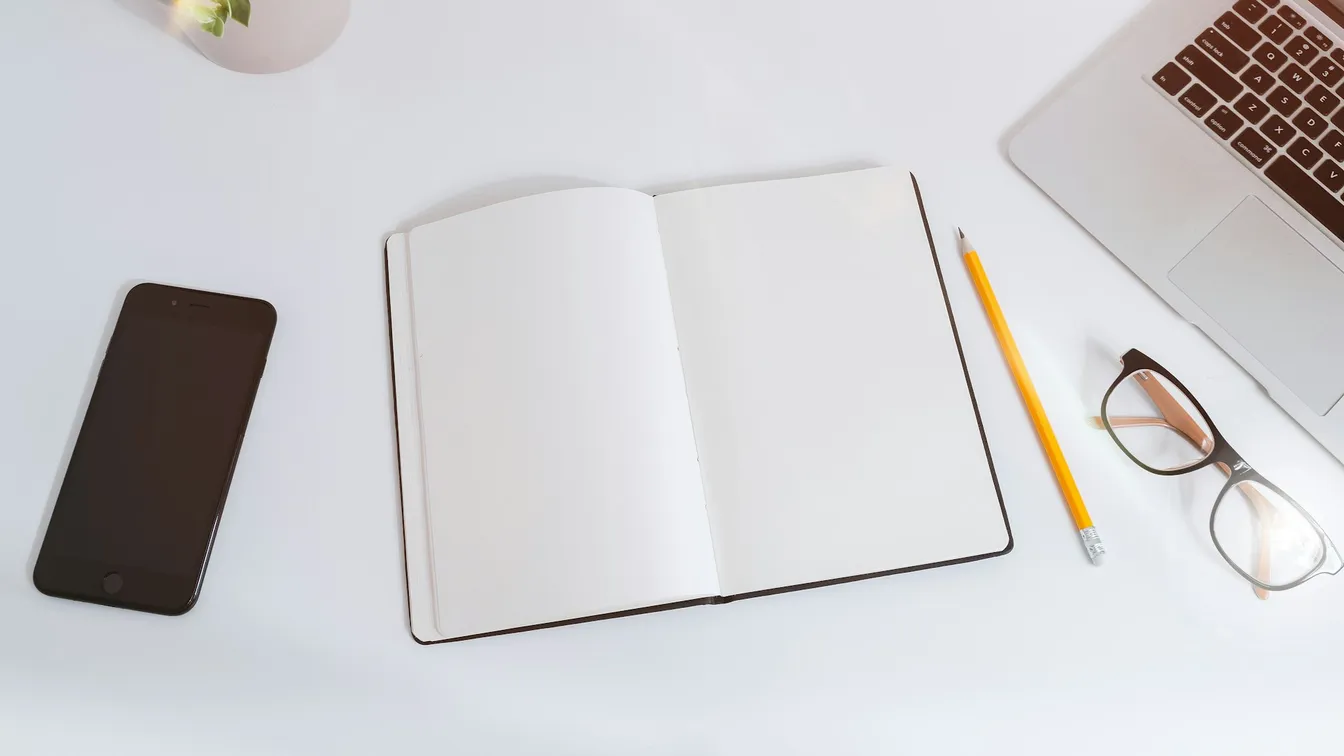 a notebook, phone, and glasses are on a white table