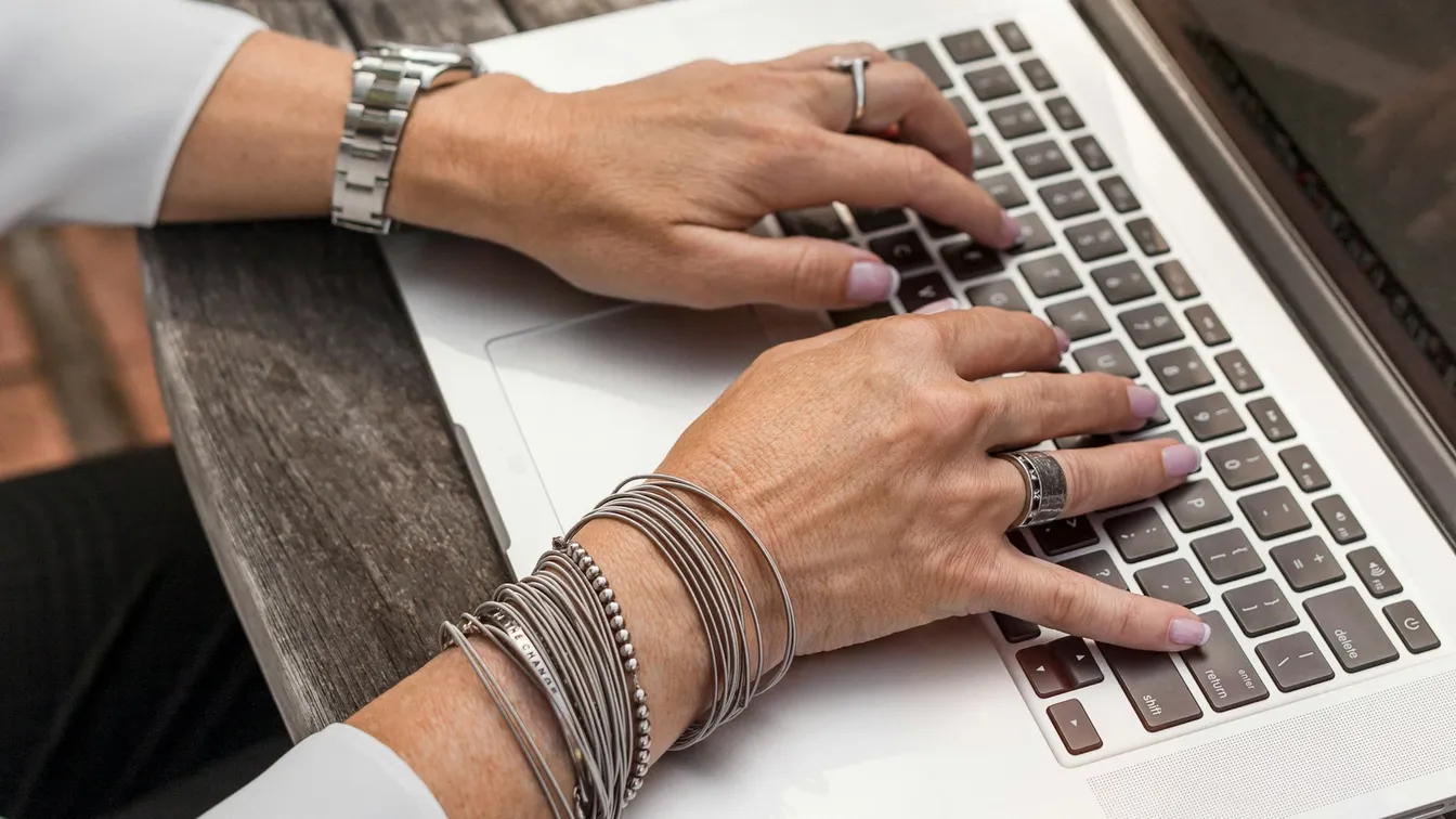 a woman typing on a laptop with bracelets on her wrist